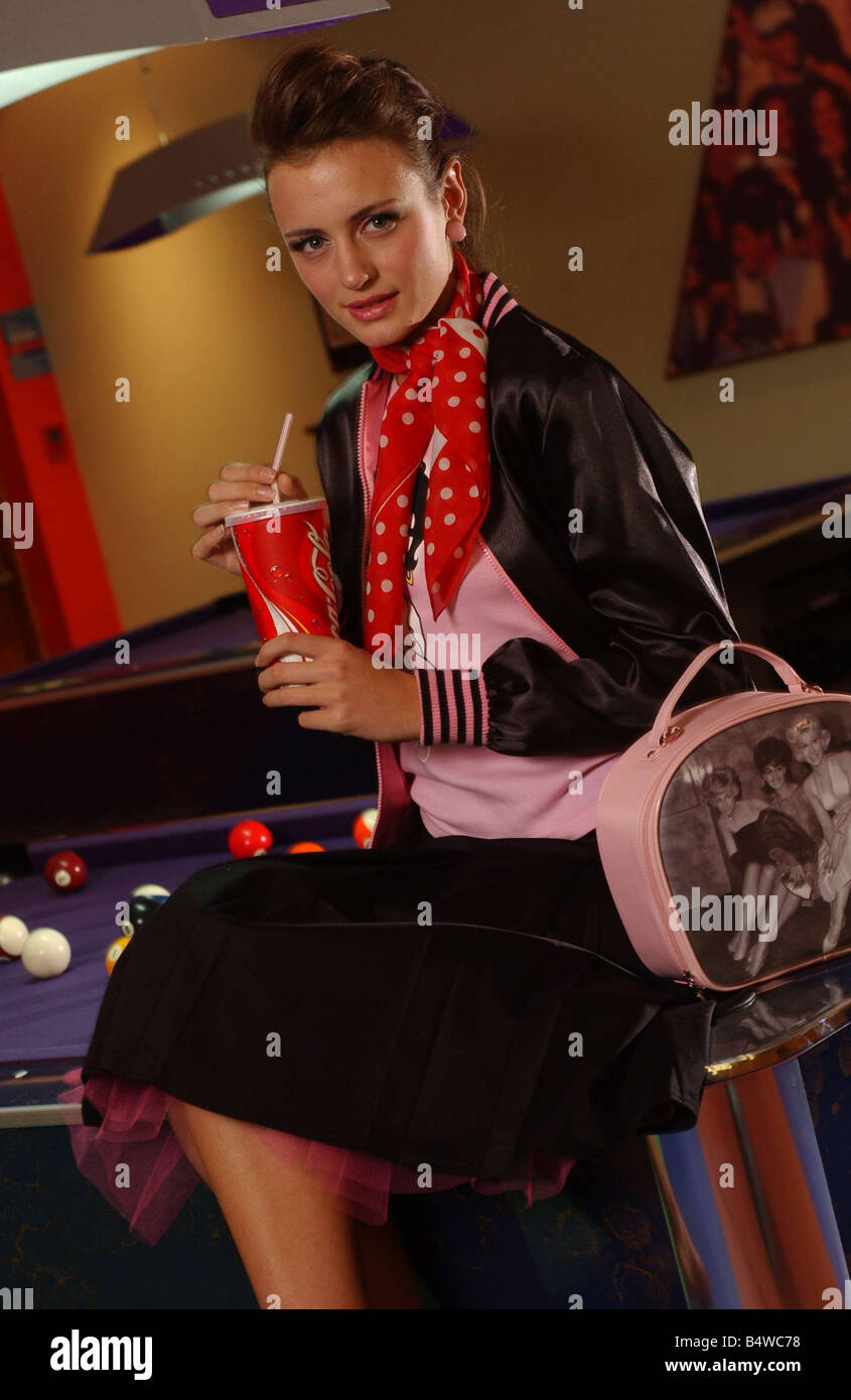 Bowling-Mode Oktober 2003 Modell Lucy Holt trägt schwarze Seide Jacke Rock mit rosa Unterrock rosa Oberteil und rot weißen Tupfen Schal um Hals Coca Cola trinken sitzen auf Billardtisch 1950s 1950 gebunden fünfziger Jahre Stockfoto