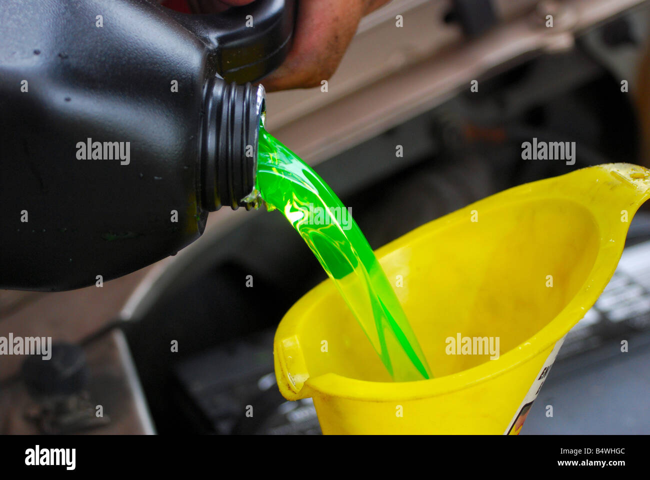 Leuchtend grüne Kühlerschutzmittel in einen gelben Trichter gegossen Stockfoto