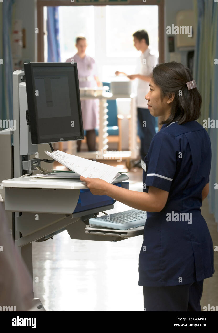 Eine Stationsschwester lächelt, als sie "Kühe", Computer auf Rädern, in eine Akutversorgung Einheit verwendet. Stockfoto