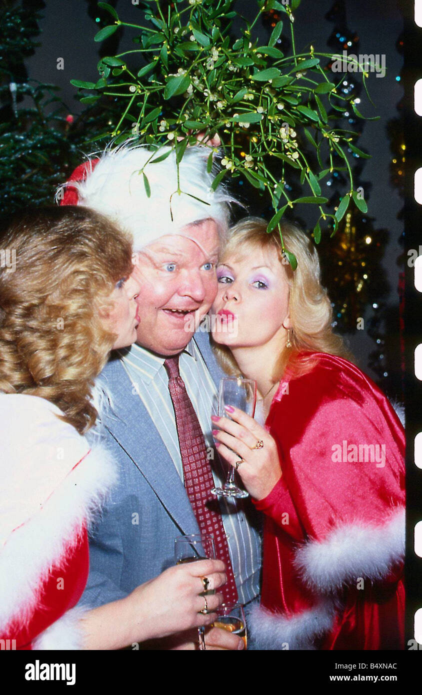 Benny Hill Komiker 1991 wird von zwei Mädchen tragen Weihnachtsmann Outfits mit Glas unter Mistelzweig geküsst Stockfoto