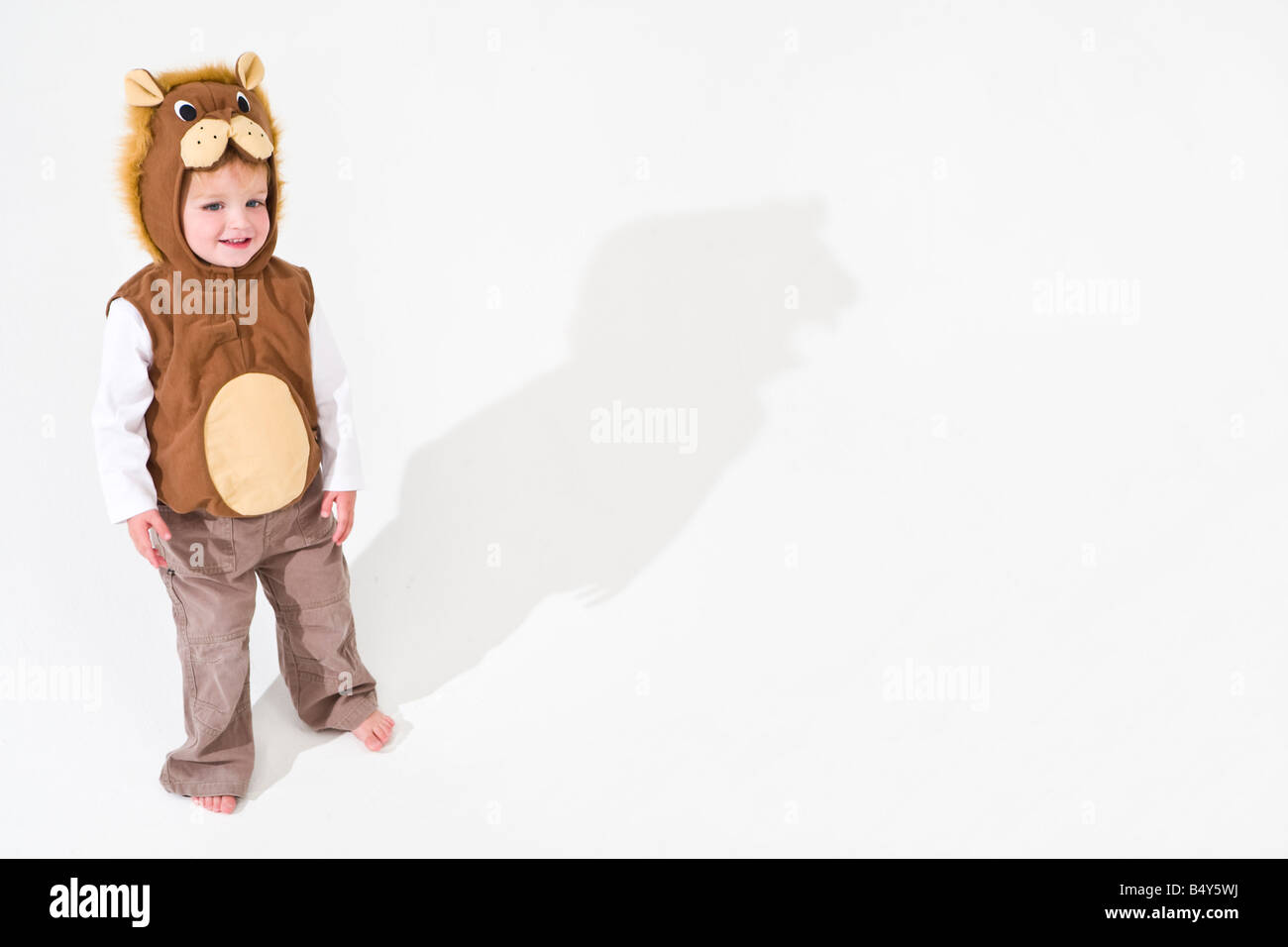 Studioaufnahme eines kleinen blonden Jungen gekleidet wie ein Löwe mit einem großen Schatten hinter ihm ausstrecken Stockfoto
