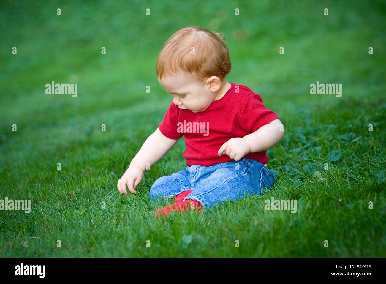 Junge rothaarige junge draußen auf dem Rasen sitzen Stockfoto