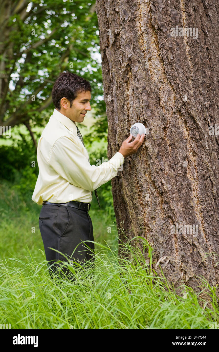 Ein gemischter ethnischer Herkunft Geschäftsmann Anpassung einen Thermostat an einem Baum außerhalb Stockfoto