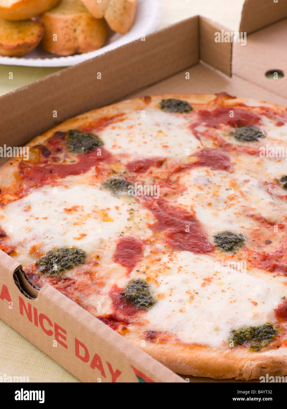 Käse, Tomaten und Pesto Pizza In A Take Away Box mit Knoblauchbrot Stockfoto