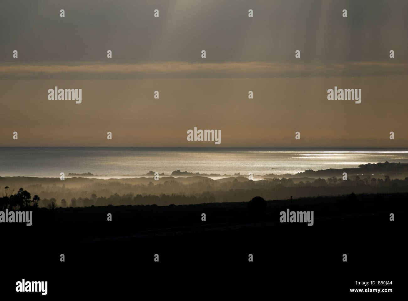 Himmlische Sonnenstrahlen durchbrechen Wolken und Licht auf dem Wasser. Wellen von Licht reflektiert auf dem Ozean vor Sonnenuntergang. Stockfoto