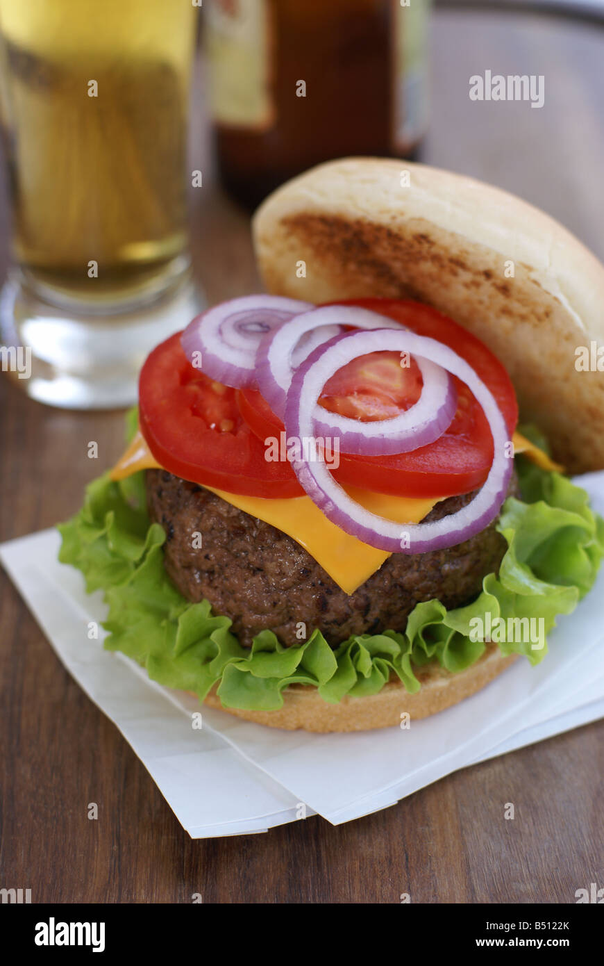 Käse-Burger mit Salat, Zwiebeln und Tomaten und ein Glas Bier Stockfoto