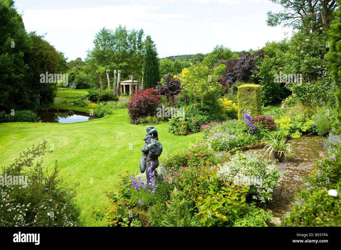 großer Garten mit gut bepflanzten Betten und eine Bronzestatue Stockfoto