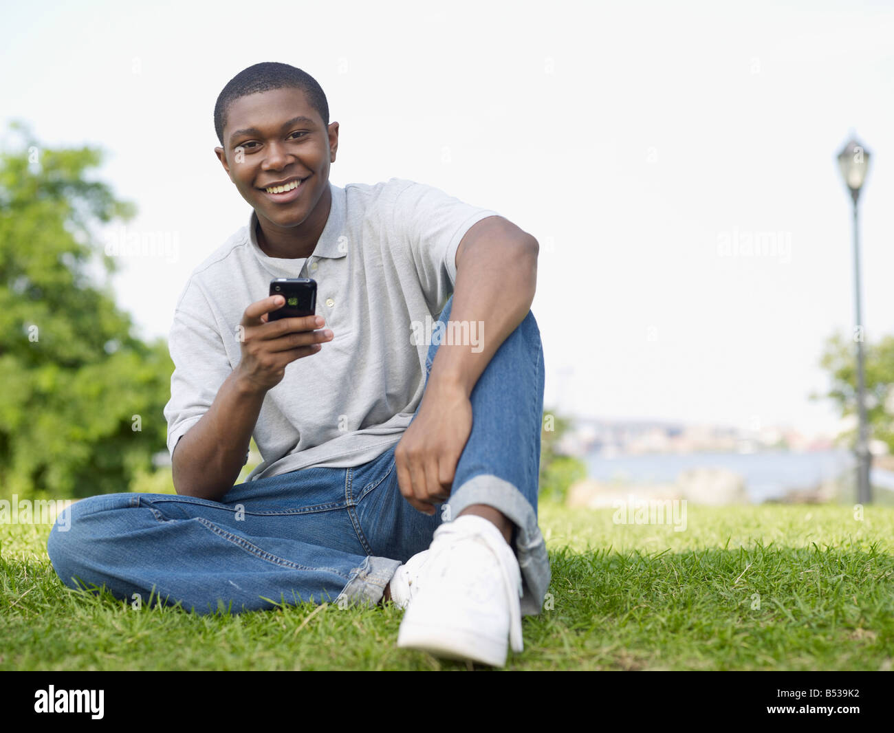 Afrikanischer Mann sitzt im Park-SMS auf Handy Stockfoto