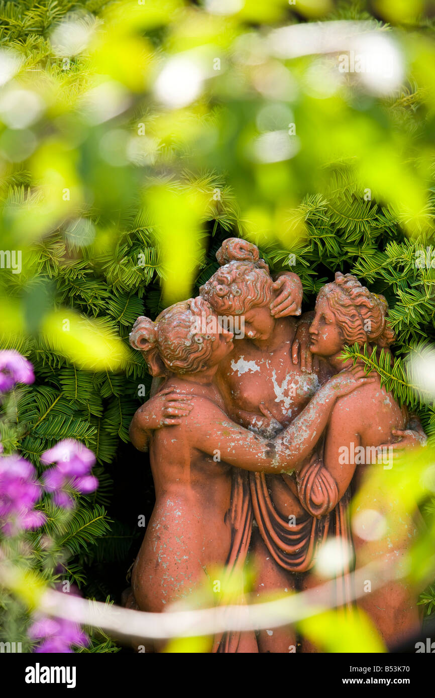 Terrakotta-Statue von drei Damen durch eine Taxushecke Stockfoto