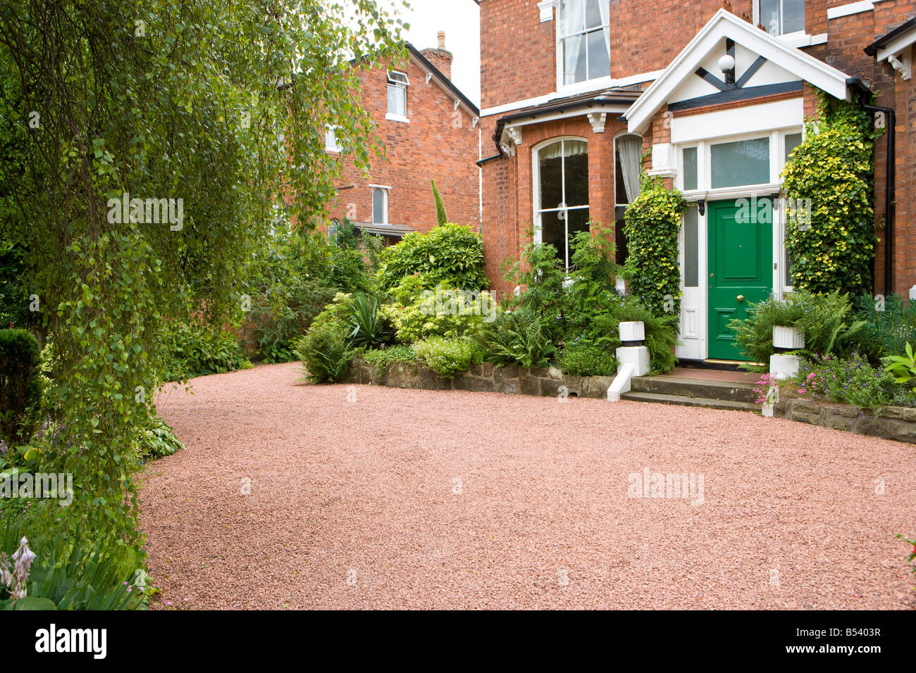 Vorgarten eines großen Einfamilienhauses mit roten Kies Einfahrt und Holly Büsche Stockfoto
