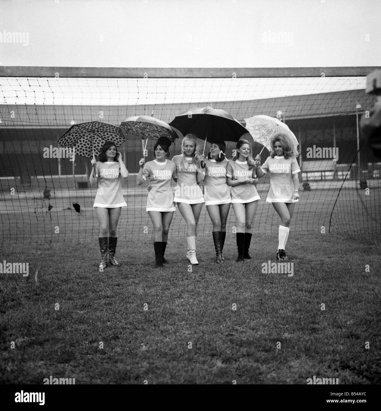 Aufgereiht in ihren Mini-Fußball-Kleidern auf was sollte die Zeit zum Anpfiff sind 6 der Scheuklappen Utd Fußball-Nationalmannschaft gewesen. Die Scheuklappen Utd V alle Sterne XI Fußball Benefizspiel hatte abgesagt, nachdem entschieden wurde, dass das Wetter nicht geeignet war, zu spielen. Als die Männer beobachtete lief die Mädchen rund um den Boden zu Manchesters Belle Vue tragen Regenschirme, um ihr Haar zu schützen. ; November 1969; Z10898 Stockfoto