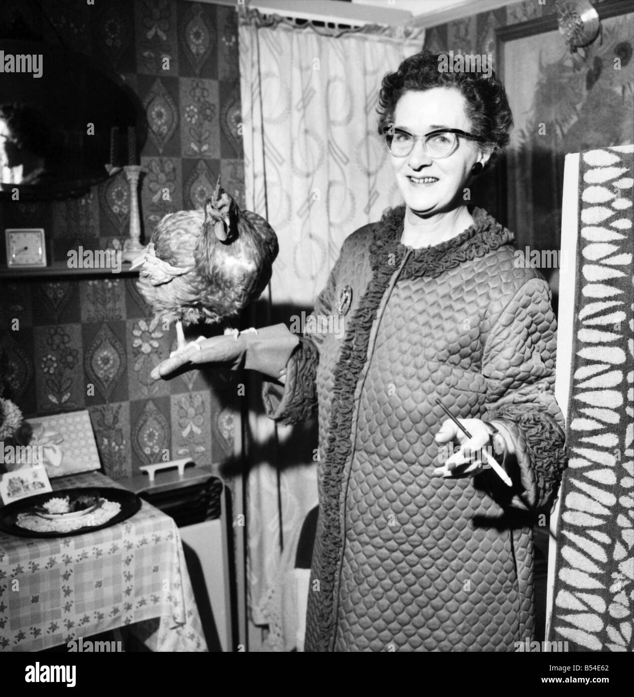 Personen: Humor: Frauen: Frau zu Hause ein Huhn in einer Hand halten und Rauchen eine Zigarette mit dem anderen. November 1969 Stockfoto