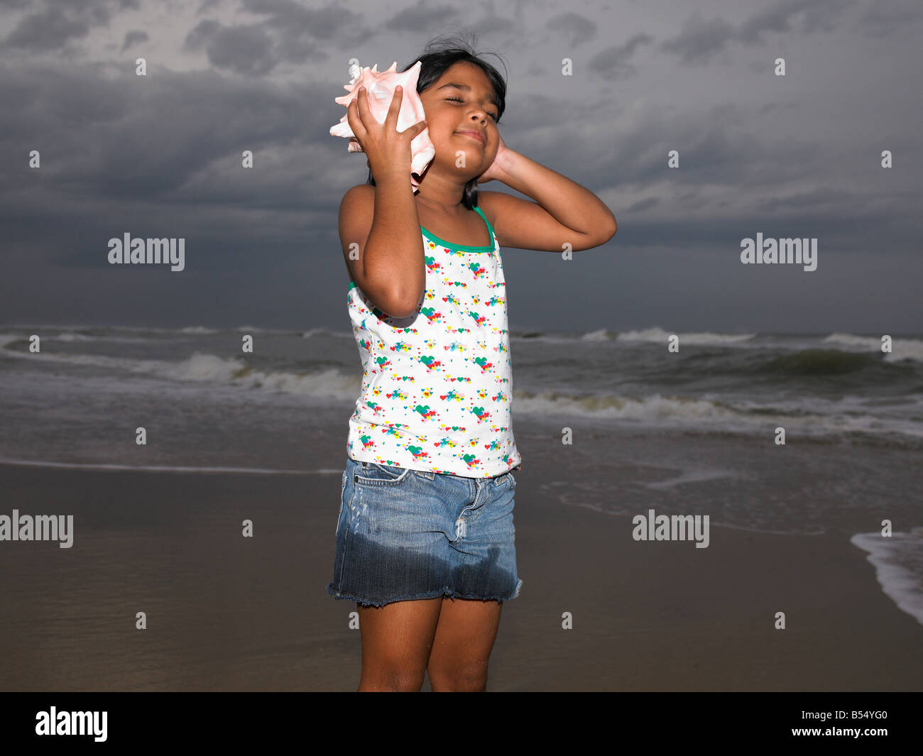 eine hübsche Asiatin indischer Herkunft anhören einer Muschel Stockfoto