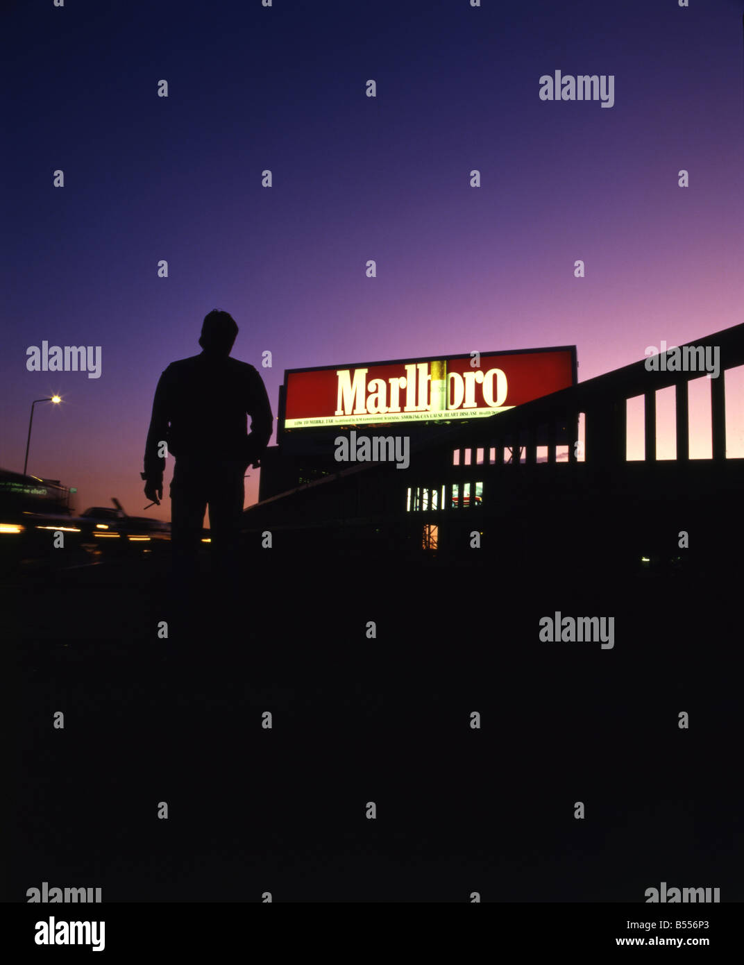 Silhouette eines Mannes mit einer Zigarette zu Fuß in Richtung einer Marlboro beleuchteten Werbetafel Stockfoto