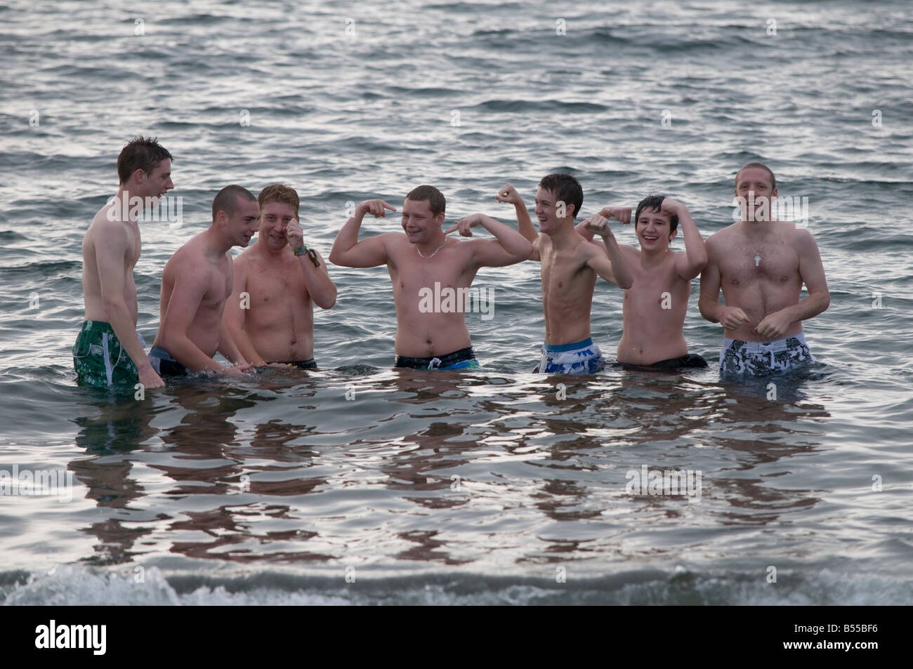 Gruppe von 7 sieben junge Männer tragen Badeanzüge stehen im Meer glücklich und lächelnd; Sommerurlaub, Wales UK Stockfoto