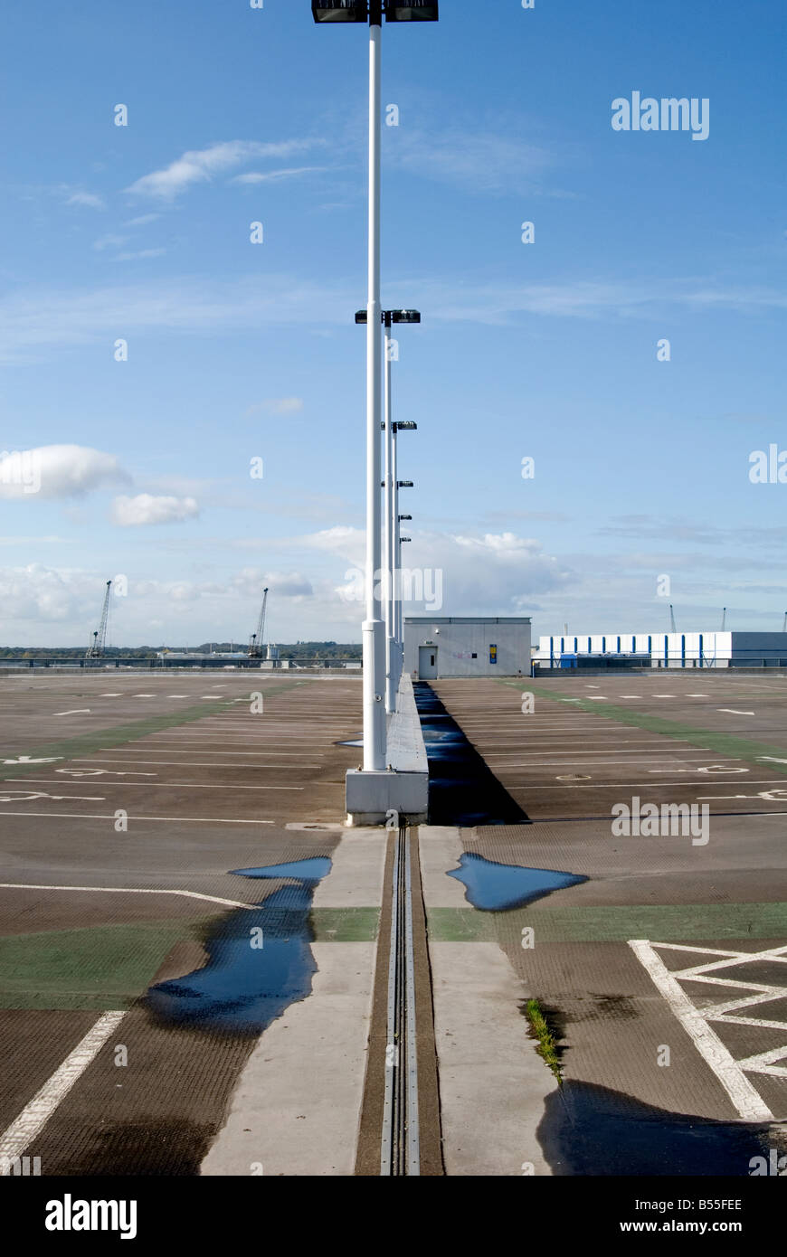 Eine Reihe von Laternenmasten auf der obersten Ebene von einem leeren Parkplatz in Southampton mit Pfützen, blauer Himmel und Wolken Stockfoto