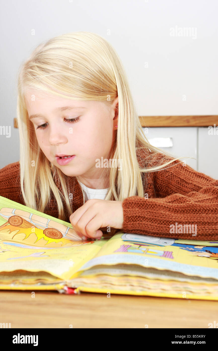 Young blonde erste Klasse Mädchen ein Buch für ihre Hausaufgaben Stockfoto