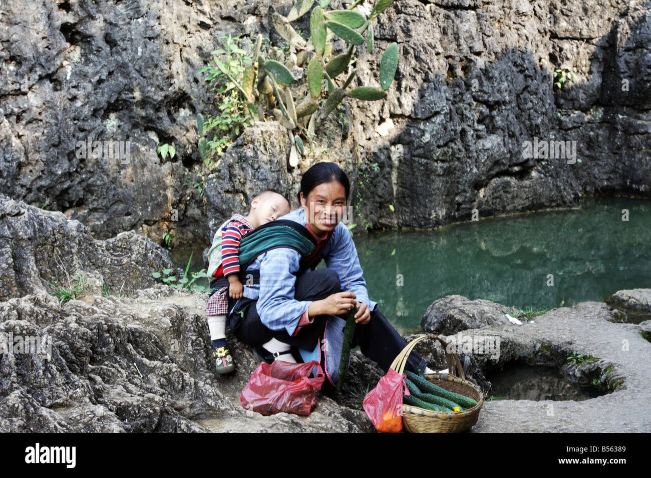 Frau der Buyi oder Buyei Minderheit mit ihrem Baby Verkauf von Gurken in der Provinz Guizhou, China Stockfoto