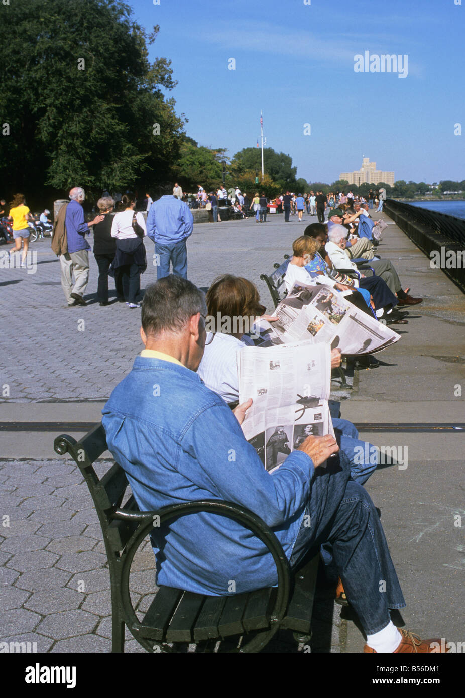 New York City Carl Schurz Park Sonntag Nachmittag Wochenende Menschen Sitzen, die Zeitung auf einer Promenade in einem Publikum zu lesen parken Stockfoto
