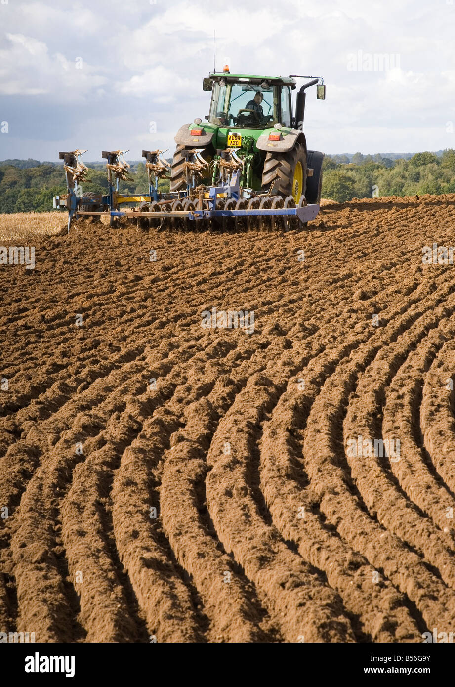 Ein Bauer mit seinem Traktor auf ein Feld mit einer Furche Pflügen befestigt UK Stockfoto