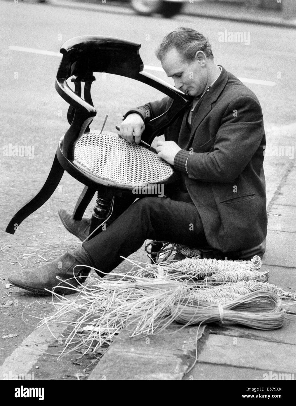 Chair Caning: Ein ungewohnter Anblick in London das alte Handwerk der Stuhl Mr John Browning 38 jährige von Battersea, Reparatur einen Rohrstock Stuhl, sitzt auf dem Rand der Fahrbahn, an der Ecke der Ladbroke Grove Rohrstock. Er erlernte das Handwerk von seinem 65-jähriger Schwiegervater, der es sein ganzes Leben lang getan hat. Er reist durch London und bekommt Arbeit auf Empfehlung. Januar 1971 P004943 Stockfoto