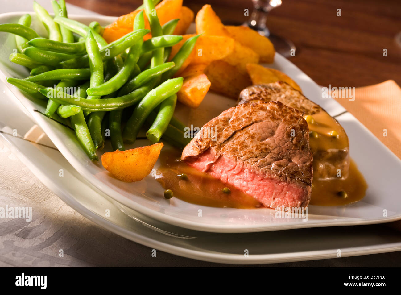 Mahlzeit mit gebratenen Rinderfilet in Pfeffersauce, grünen Bohnen und Kartoffelspalten Stockfoto