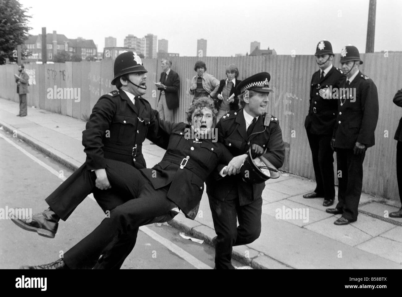 Lewisham Riot 1977: Ein verletzter Polizist wird von Kollegen von das Lewisham Riot getragen. Der Aufstand wurde ausgelöst von einer nationalen Front Marsch durch das Zentrum der Stadt, die durch eine linke Zähler Demonstration konfrontiert wurde. August 1977 77-04357-014 Stockfoto