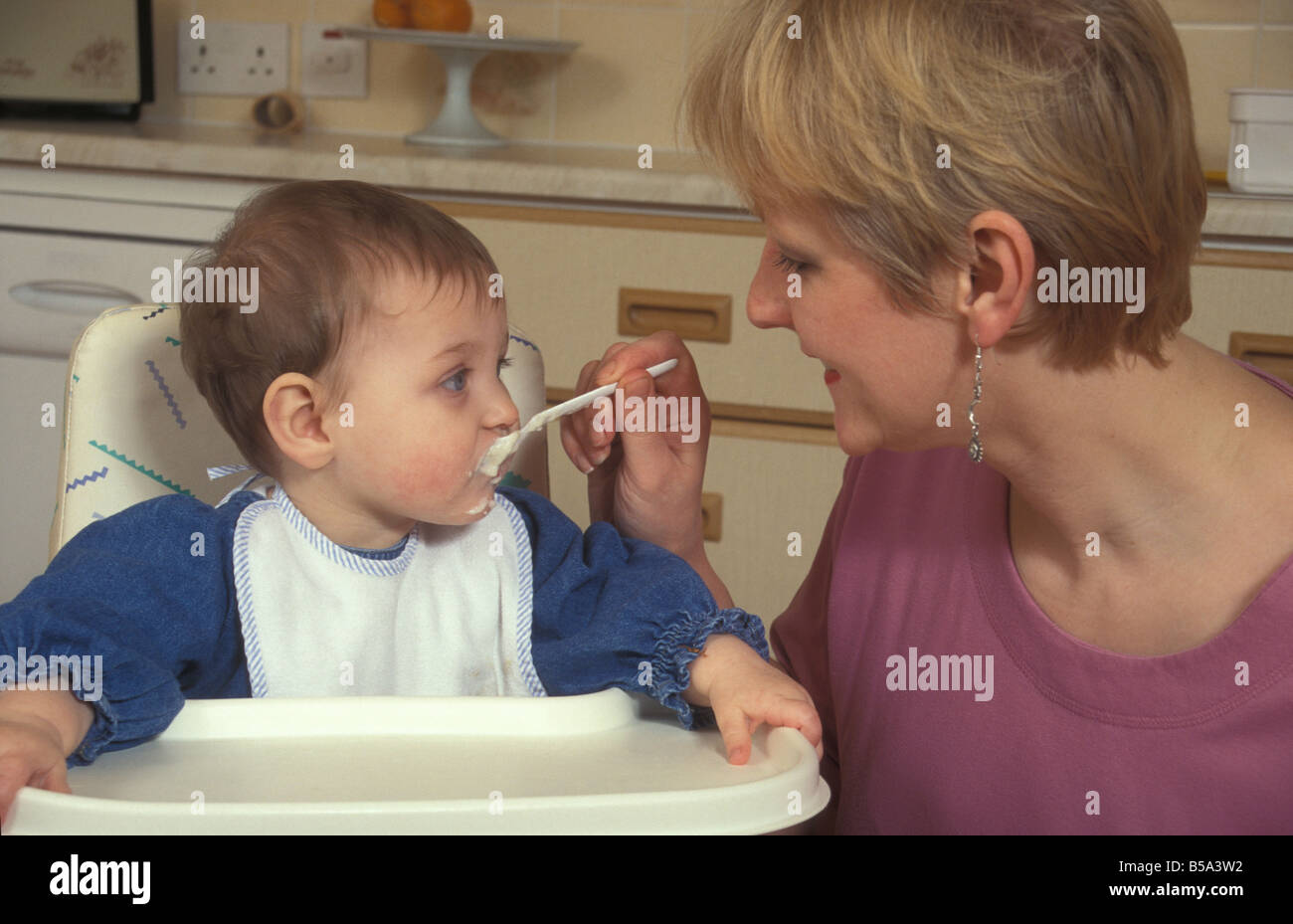 Frau oder Mutter Spoonfeeding Baby im Hochstuhl Stockfoto