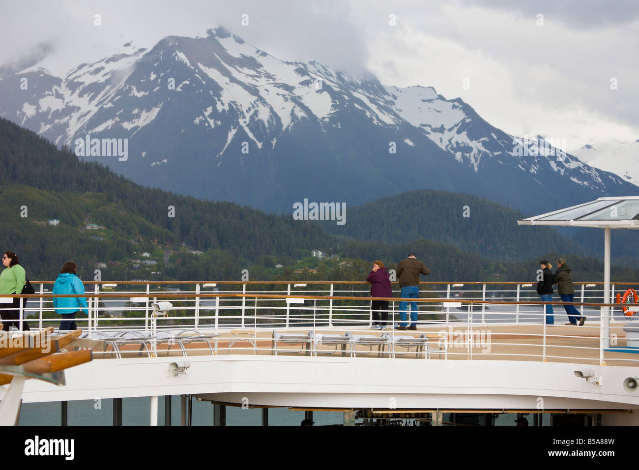Kreuzfahrtpassagiere, die am Schiffsgeländer stehen und die schneebedeckten Berge in der Nähe von Sitka, Alaska, bestaunen Stockfoto