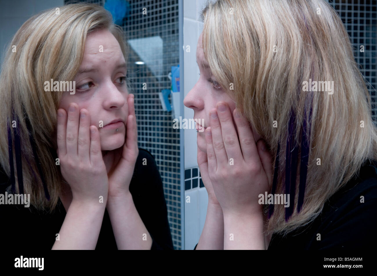 Betroffenen krank aussehende junge Frau Blick auf ihr Spiegelbild überprüfen ihr Teint und Haut Zustand im Badezimmerspiegel Stockfoto