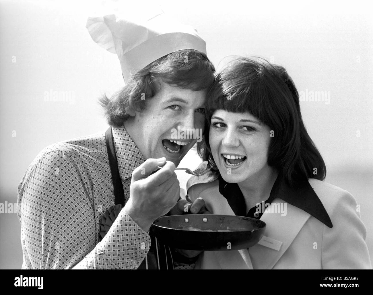 Englands Top-Mann in der Küche seine Nahrung mit einer Frau, aus der Pfanne Essen zu teilen. &#13; &#10; April 1975 &#13; &#10; 75-2138-008 Stockfoto