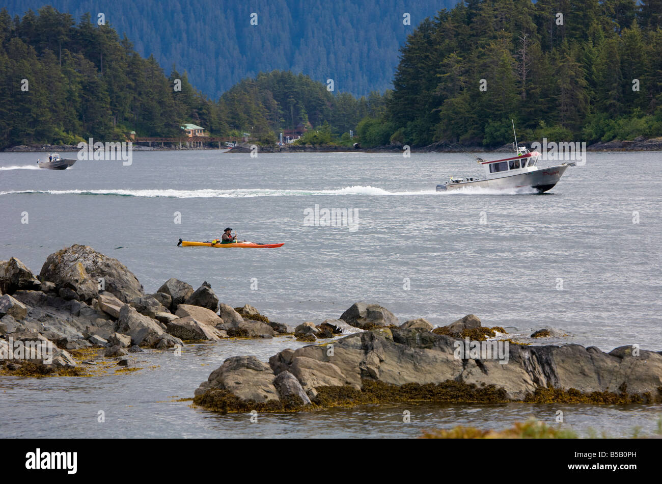 Kajak und Angelboote/Fischerboote in der Nähe von Felsenküste im östlichen Ärmelkanal der Inside Passage in Sitka, Alaska Stockfoto