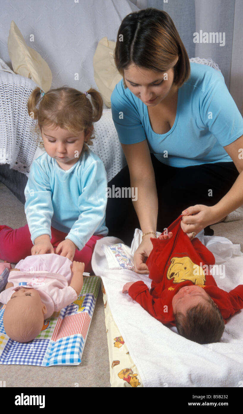 Kleinkind mit Puppe Kopieren ihrer Mutter, wie sie Babys Windel wechselt Stockfoto