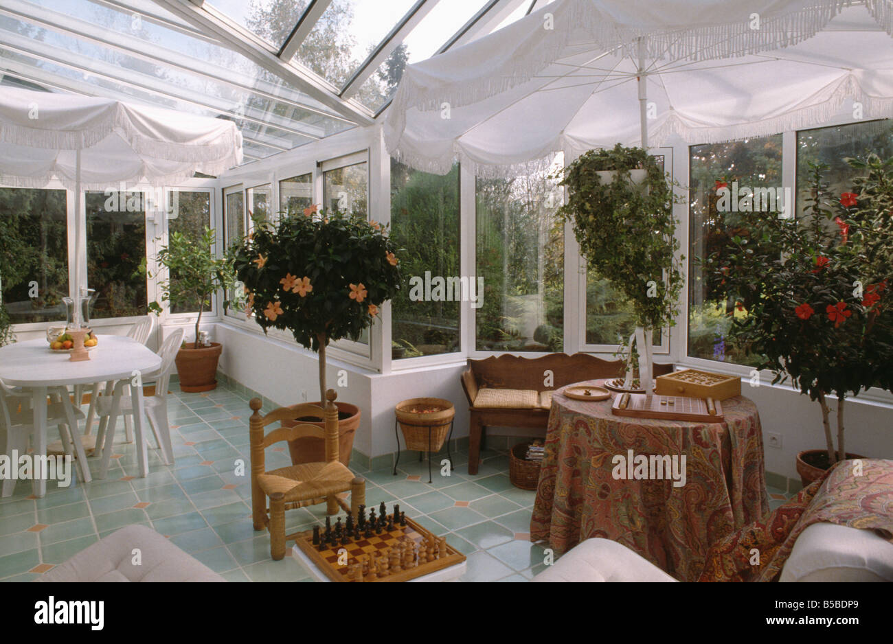 Weiße Schirme geben Schatten im Wintergarten Ess- und Wohnzimmer mit Schachspiel und Tisch mit gemusterten Tuch Stockfoto