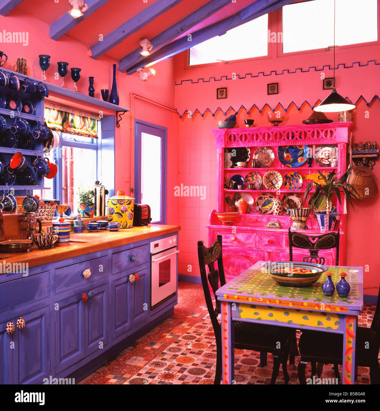 Bunt bemalten bunten Tisch in hell rosa Küche mit pulsierenden blau und  rosa Kommode und mehrfarbige Böden Stockfotografie - Alamy