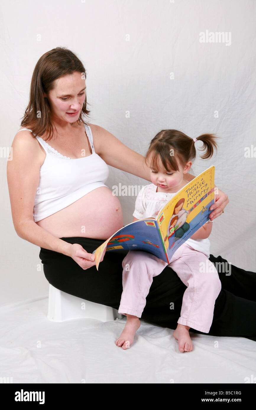 Zwei Jahre sitzt alte Tochter Säugling Kleinkind auf schwangere Mütter Schoß Kinder Buch über Schwangerschaft und immer eine große Schwester Stockfoto