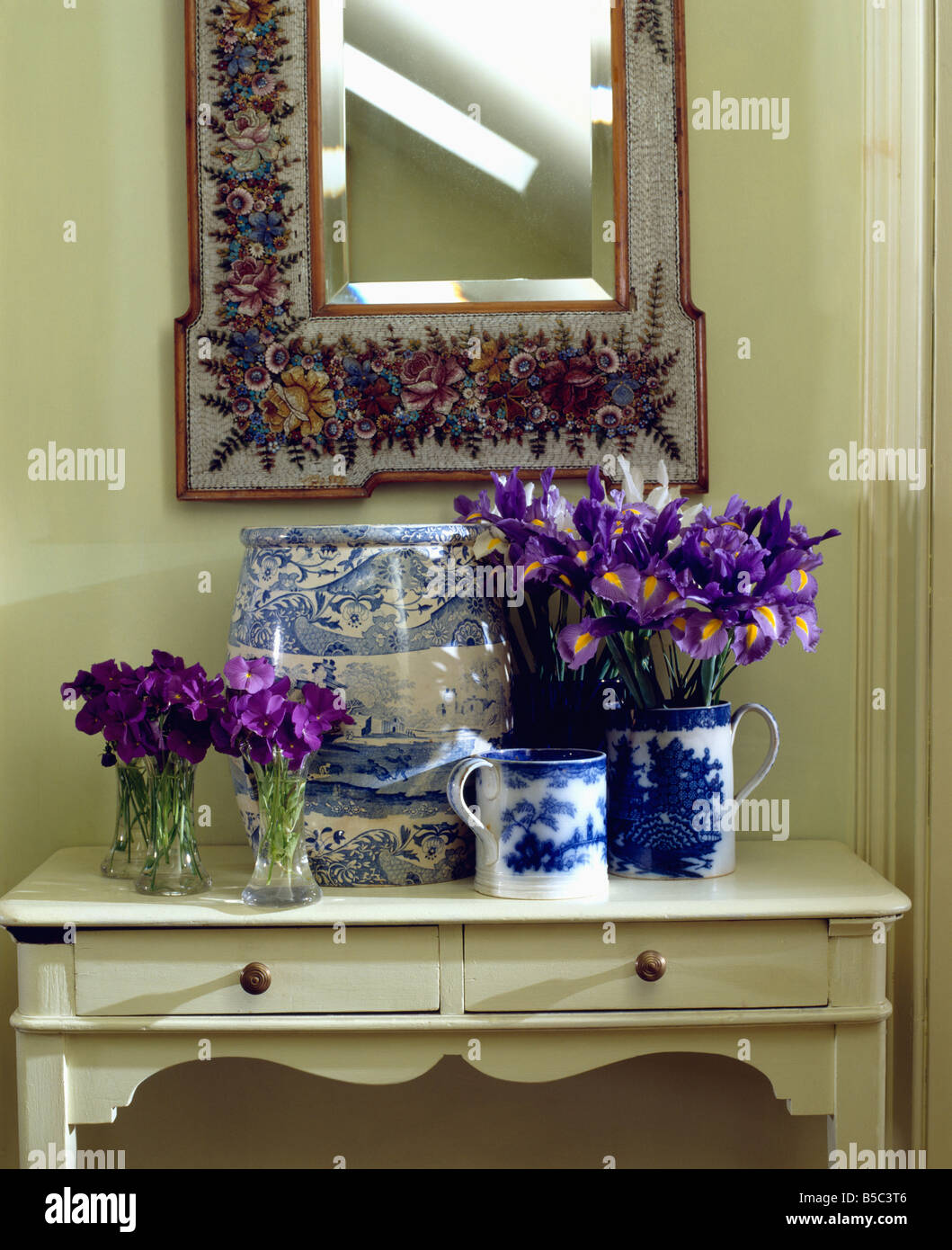 Lila Schwertlilien und Bratschen in blauen & weißen Krüge und Glasvasen auf Creme Konsolentisch unter dekorativer Spiegel Stockfoto