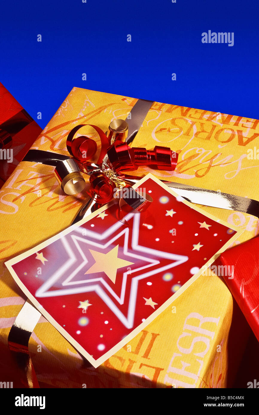 Gold metallic Bogen mit Ribbon Curl um Geschenk und gegenwärtigen Weihnachtsstern auf rote Karte blau Hintergrund gebunden Stockfoto
