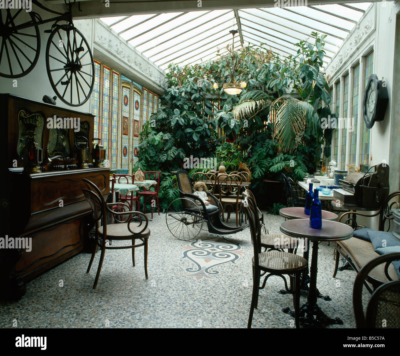 Antiker Thonet Bugholzstühle und rechnen mit kleinen Tischen im Wintergarten mit üppigen Zimmerpflanzen und Terrazzo-Boden Stockfoto