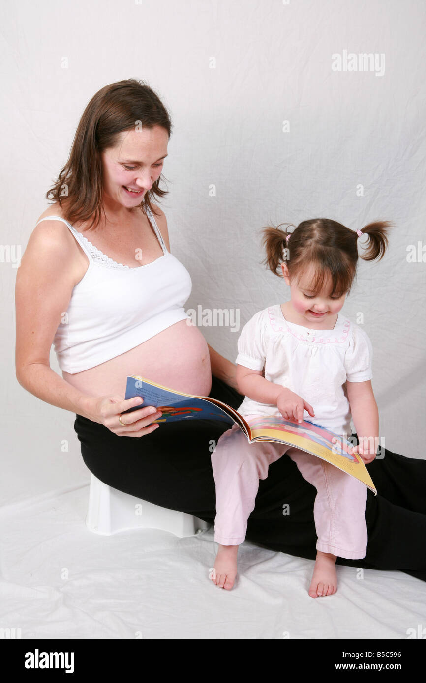 Zwei Jahre sitzt alte Tochter Säugling Kleinkind auf schwangere Mütter Schoß Kinder Buch über Schwangerschaft und immer eine große Schwester Stockfoto