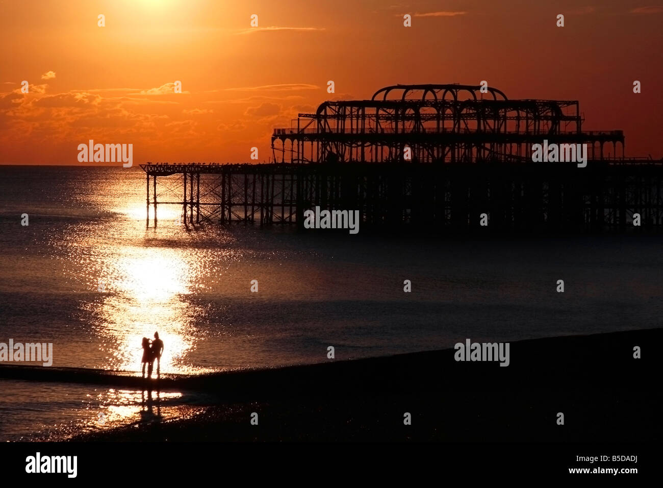 Romantischer Sonnenuntergang über Brightons West Pier mit zwei Personen im Vordergrund Stockfoto