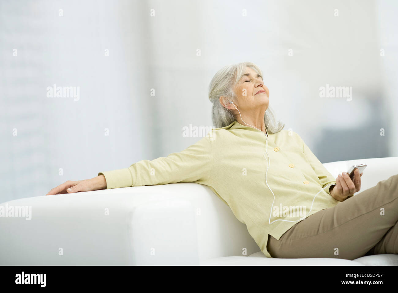 Ältere Frau Musik anhören, auf Couch sitzen mit geschlossenen Augen Stockfoto