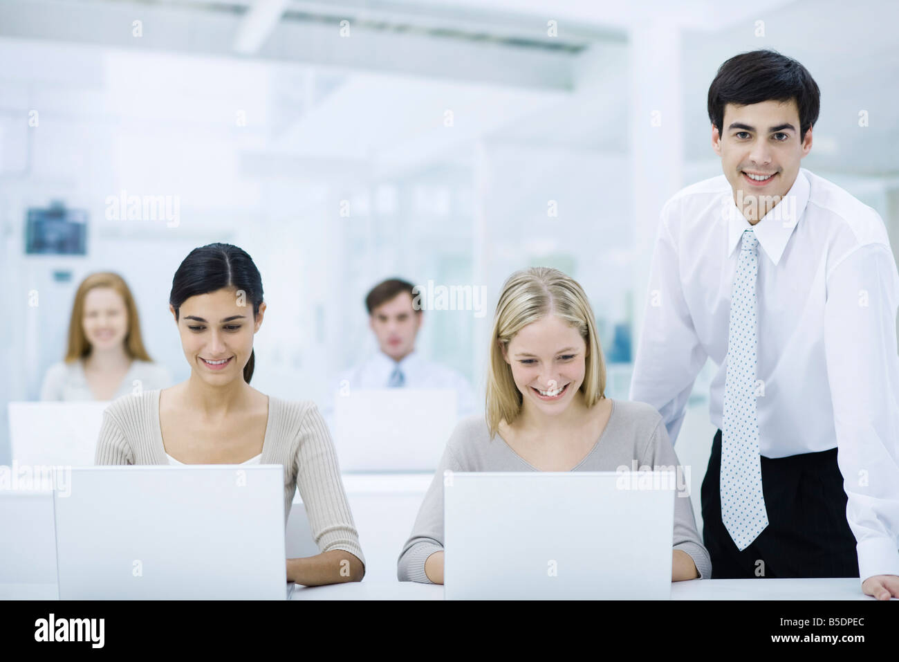 Betreuer stehend neben Beschäftigten auf Laptops, lächelnd in die Kamera Stockfoto