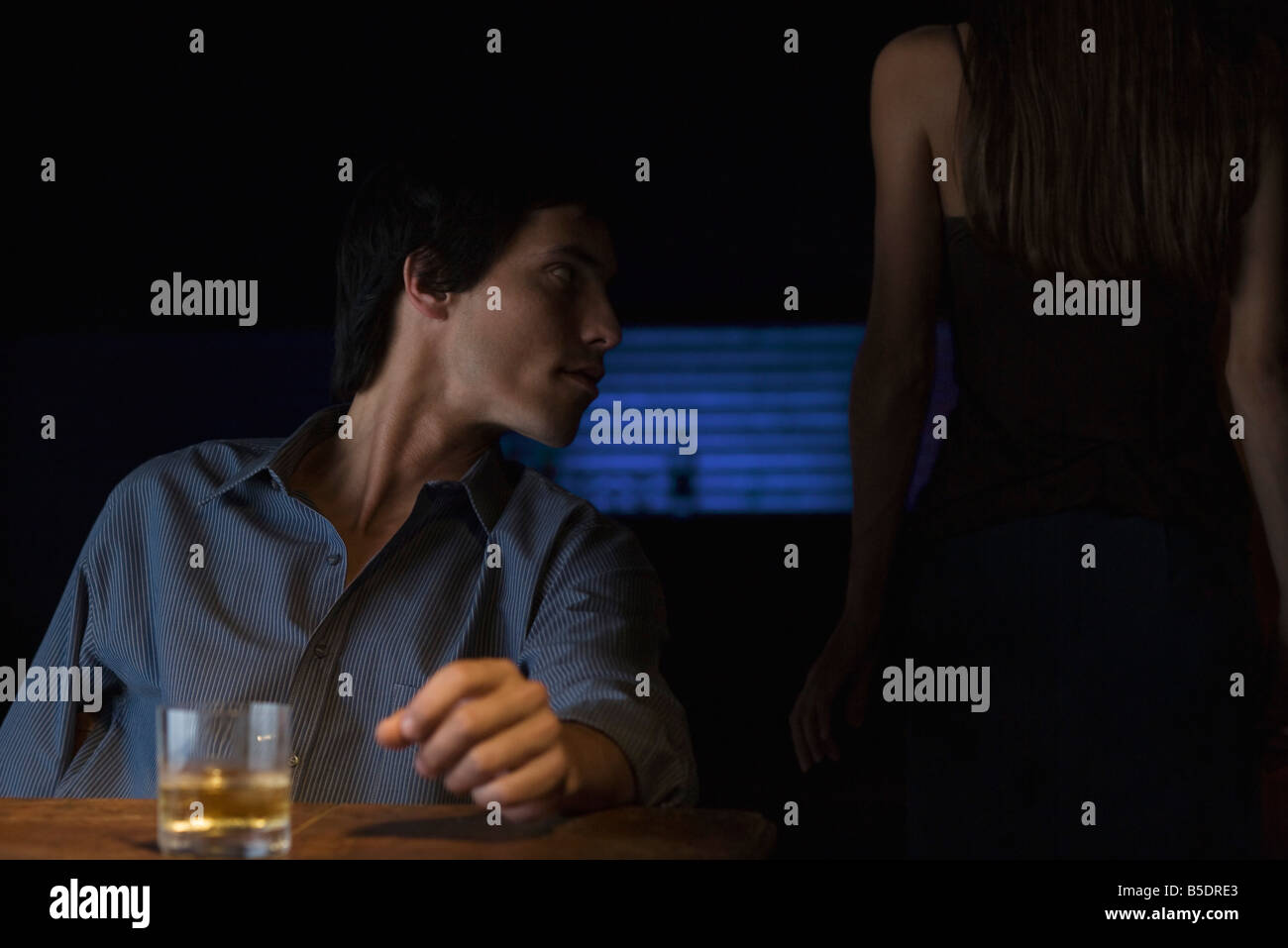 Glas Whiskey auf Tisch, Mann, sitzen und schauen Weg, hintere Ansicht der Frau im Dunkeln Stockfoto