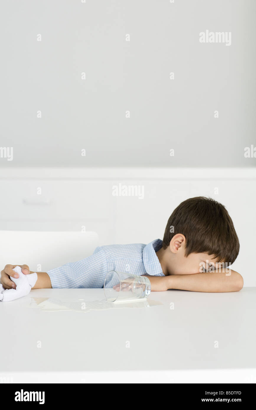 Junge sitzt am Tisch mit verschüttete Milch, Kopf nach unten, halten Handtuch Stockfoto