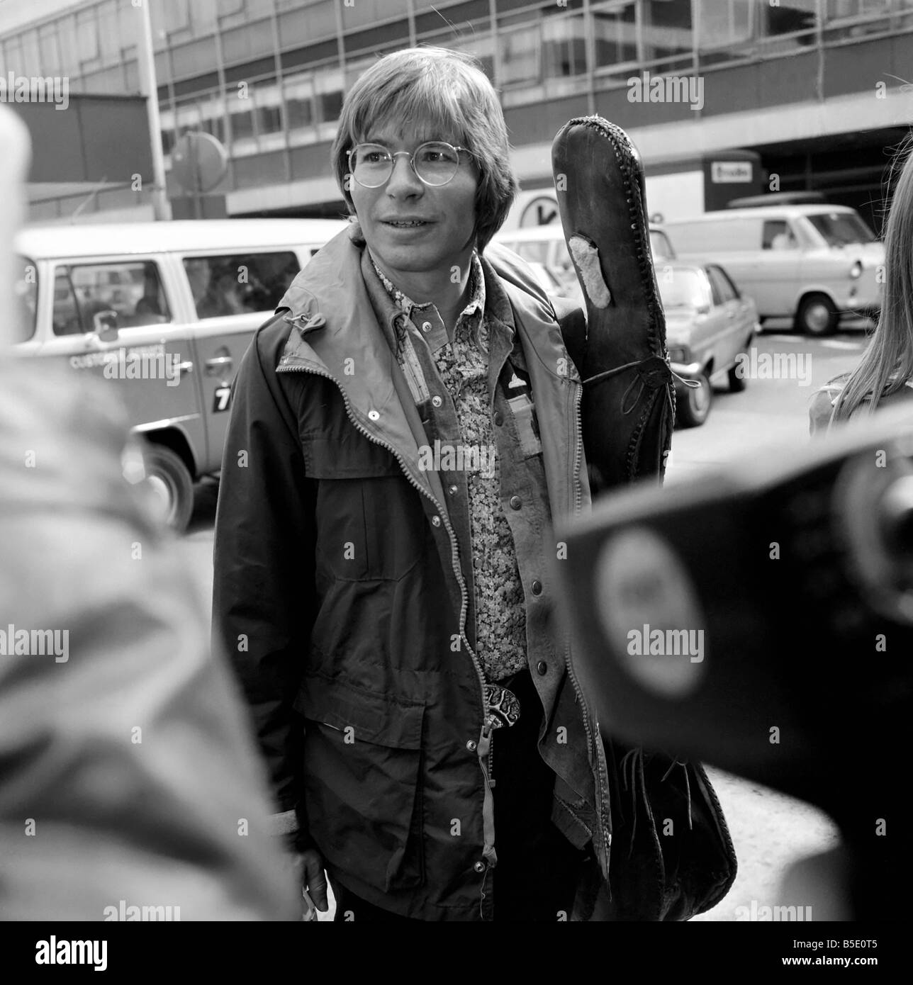 John Denver: US-Sängerin gesehen hier in London am Flughafen mit seiner Gitarre. April 1976 Stockfoto