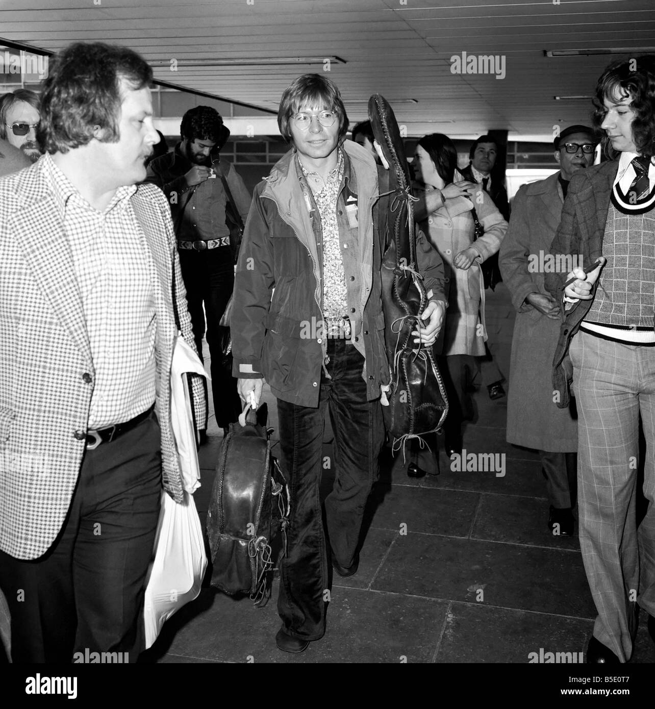 John Denver: US-Sängerin gesehen hier in London am Flughafen mit seiner Gitarre. April 1976 Stockfoto