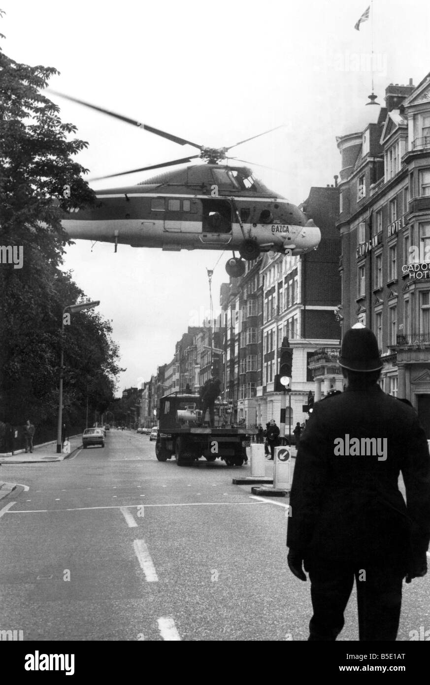 Guten Morgen-Officer, wird nicht sein A Minute: ein Polizist hält eine sorgfältige Uhr als ein Hubschrauber schwebt niedrig über Londons Belgravia. Der Helikopter sank auf um drei riesigen Generatoren auf das Dach des Hotel Carlton Towers zu hissen. Mit einem gigantischen Kran würde die Operation drei Tage und verursacht Verkehrschaos Marmeladen haben. Die Luftbrücke am Sonntagmorgen (30.09.73) nahm nur zwölf Minuten und niemand bekam einen Parkschein lösen. Oktober 1973 P001039 Stockfoto