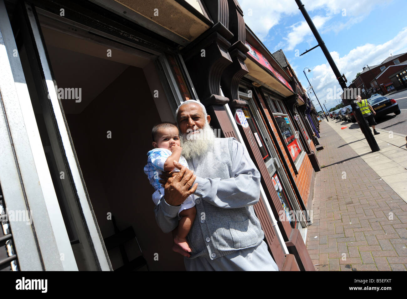 Ein Einwanderer hält Opa seinem Enkel vor seinem Geschäft in der Innenstadt Bolton, UK Stockfoto