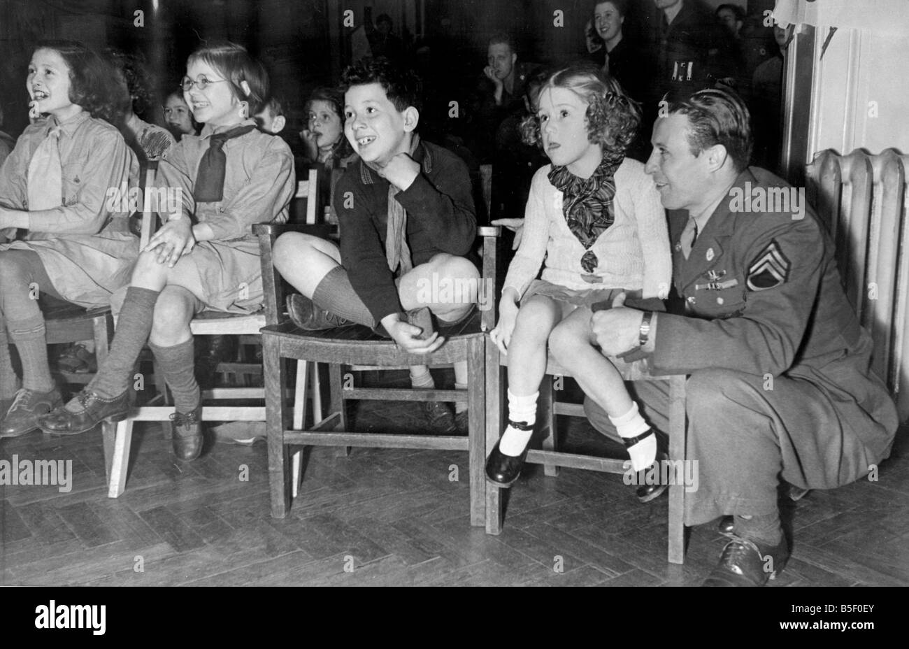 US-Armeesoldaten feiern die großen amerikanischen Thanksgiving Day Festival im Columbia Club in London durch unterhaltsame Kinder aus dem East End ein Soldat beobachtete einen Mickey-Mouse-Film mit den Kindern sitzen auf Holzstühlen November 1943 Stockfoto